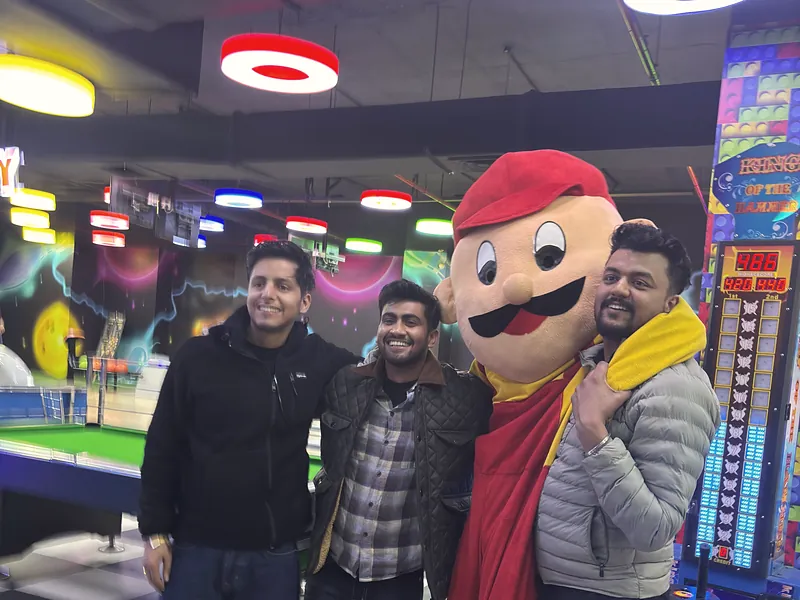 Three colleagues with a costumed mascot at an arcade