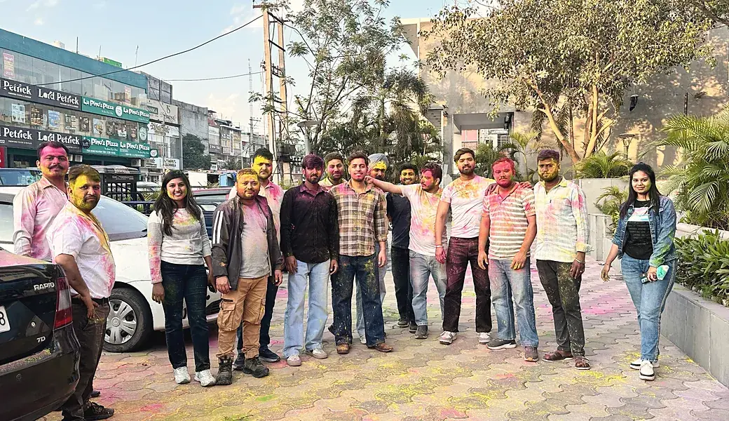 The team outdoors, faces and clothes covered in Holi colour